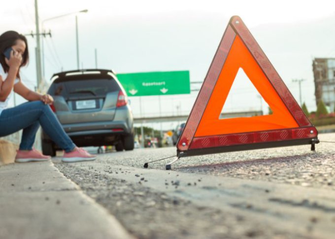 Kobieta po ustawieniu trójkąta ostrzegawczego na autostradzie bezpiecznie czeka na pomoc